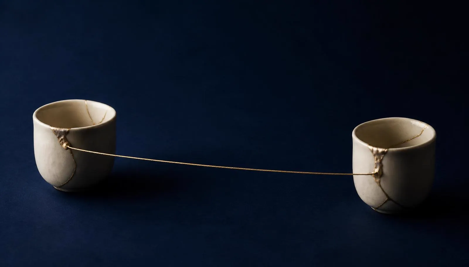 Deux tasses en céramique ivoire reliées par un fil doré tendu, sur fond bleu nuit